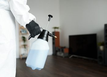 Close-up of cleaning worker in protective suit using sprayer with detergent while doing housework